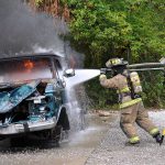 Two firefighters extinguishing a controlled fire using a water hose.