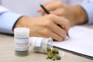 Doctor writing prescription and bottle with medical cannabis on table close up