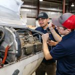 Two students in the aviation program doing maintenance on a plane engine